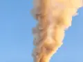 Gęsty, brązowawy dym unosi się na tle błękitnego nieba.