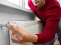 Mężczyzna w czerwonym swetrze reguluje termostat grzejnika, oszczędzając energię. To jego sposób na wykorzystanie bonu ciepłowniczy.