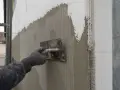 Pracownik nakłada tynk na styropian, tworząc warstwę zbrojoną siatką. Dopuszczalne nierówności na elewacji są korygowane.