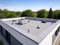 Nowoczesny dach płaski konstrukcja z elementami wentylacyjnymi i świetlikiem, otoczony zielenią.