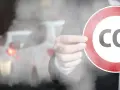 Ręka trzyma znak z napisem CO2 na tle korka ulicznego. Symbolizuje to potrzebę ograniczenia emisji, jak w przypadku certyfikatu CE dla produktów.
