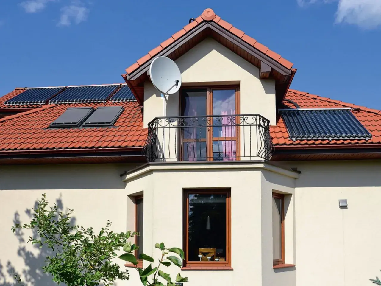 Elegancki wykusz z balkonem i oknami, na dachu panele słoneczne i antenę satelitarną.