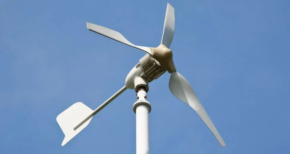 Biała elektrownia wiatrowa z trzema łopatami na tle błękitnego nieba.
