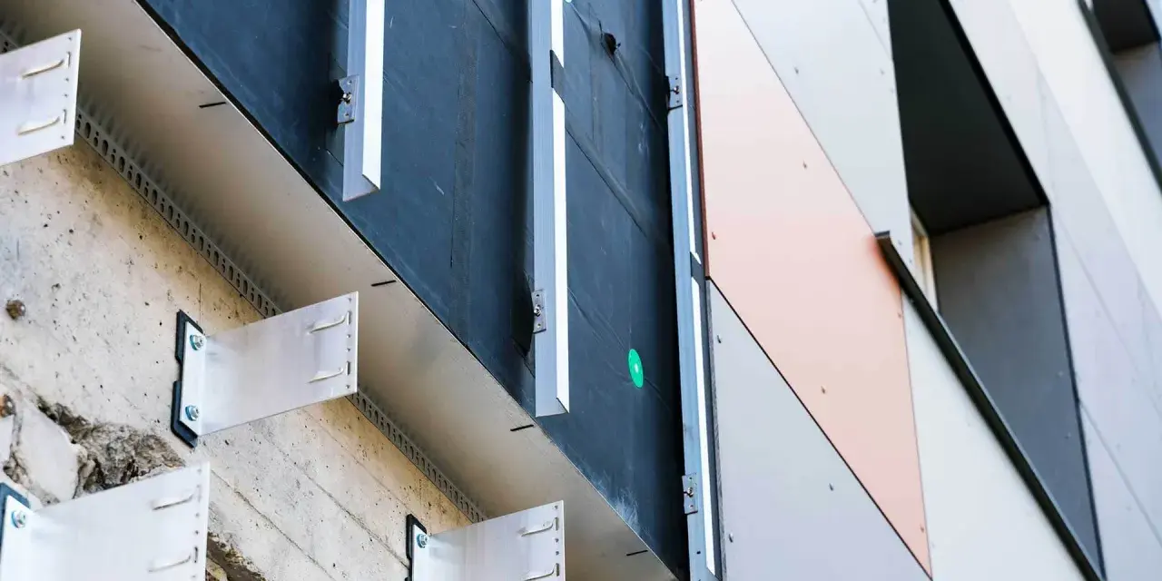 System mocowania elewacji wentylowanej. Metalowe wsporniki przytwierdzone do betonowej ściany, tworzące przestrzeń dla izolacji i wentylacji.