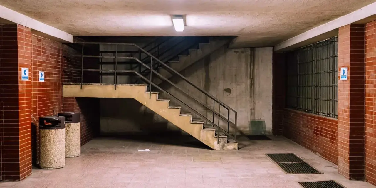 Betonowa suterena z ceglanymi ścianami, schodami i dwoma koszami na śmieci.