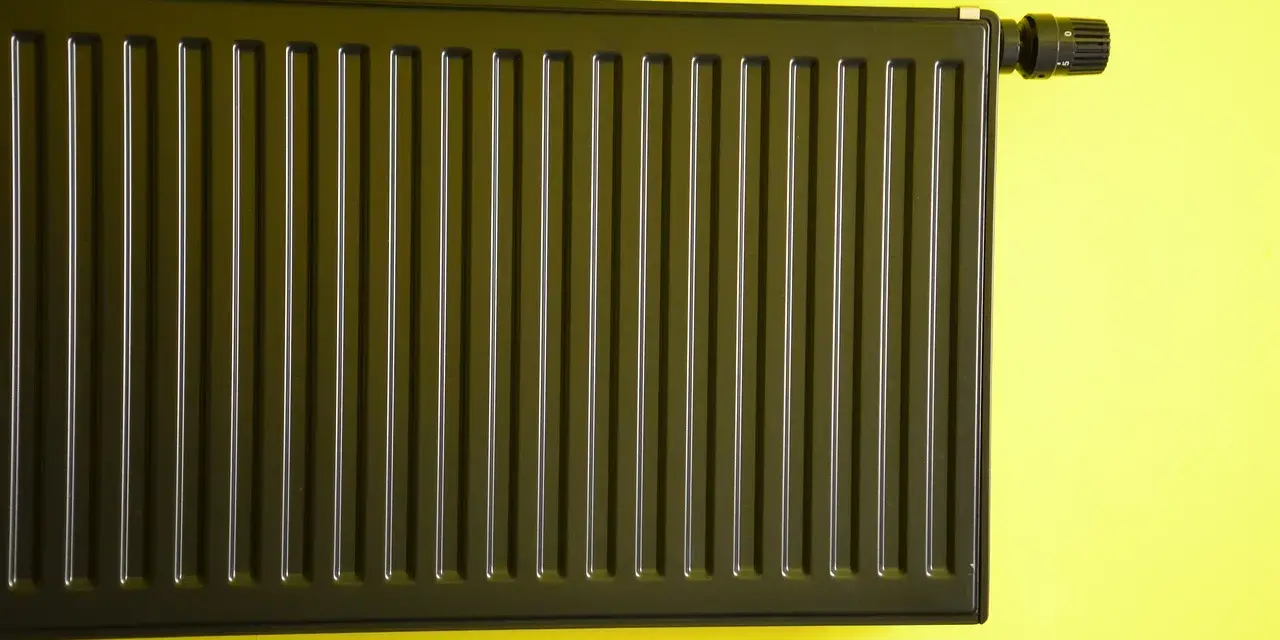 Nowoczesne malowanie grzejnika aluminiowego na ciemny kolor. Grzejnik z termostatem na żółtej ścianie.
