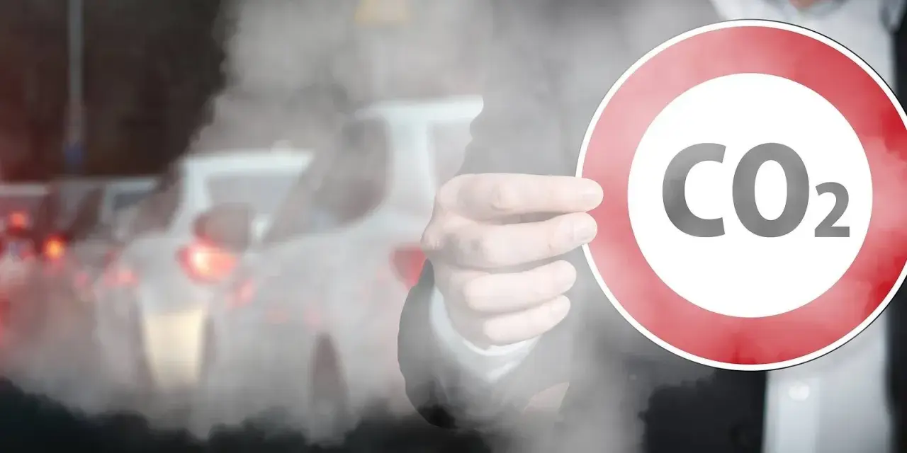 Ręka trzyma znak z napisem CO2 na tle korka ulicznego. Symbolizuje to potrzebę ograniczenia emisji, jak w przypadku certyfikatu CE dla produktów.
