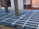 Konstrukcja pod wysoki taras z deski kompozytowej, z drzewami przechodzącymi przez ruszt.