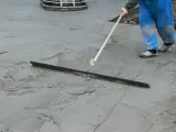 Pracownik w niebieskich spodniach wykonuje protokół wygrzewania posadzki, wygładzając świeży beton długą łopatą.