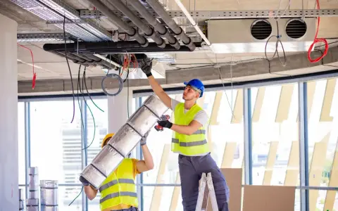 Dwóch pracowników montuje systemy HVAC, instalując izolację na rurach. To kluczowy element zapewniający komfort cieplny.
