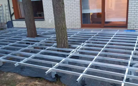 Konstrukcja pod wysoki taras z deski kompozytowej, z drzewami przechodzącymi przez ruszt.