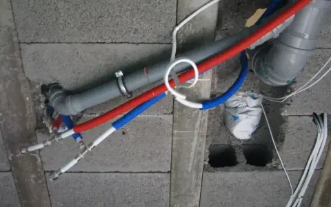 Instalacja wodna z rurami PP w ścianie z pustaków. Widoczne rury czerwone i niebieskie, szary odpływ.
