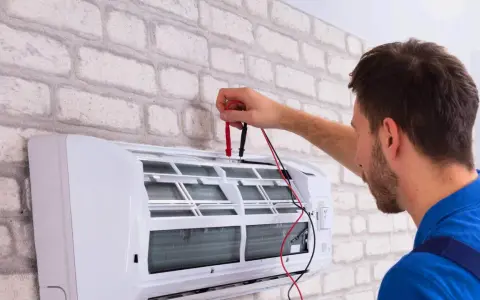 Sprawdź, jaka jest odgrzybianie klimatyzacji cena. Technik z miernikiem przy białej klimatyzacji.