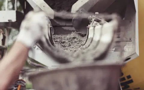 Ręka w rękawiczce kieruje strumień cementu do maszyny. Zastanawiasz się, ile kosztuje worek cementu?