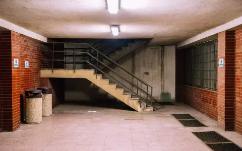 Betonowa suterena z ceglanymi ścianami, schodami i dwoma koszami na śmieci.