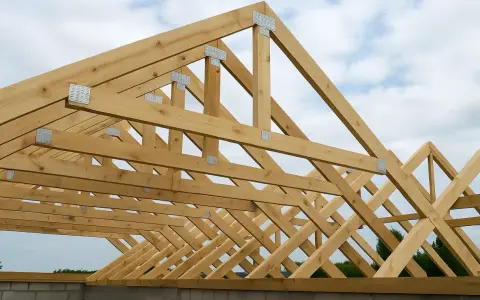 Drewniana więźba wieszarowa, konstrukcja dachu w budowie, z widocznymi metalowymi łącznikami i belkami podtrzymującymi.