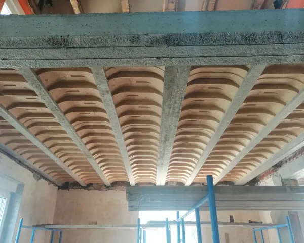 Widok od dołu na strop w domu parterowym, z widocznymi belkami stropowymi i pustakami ceramicznymi.