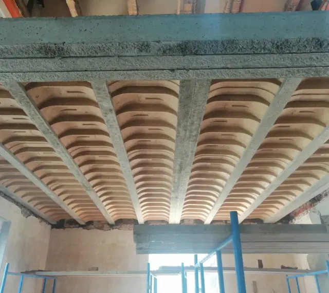 Widok od dołu na strop w domu parterowym, z widocznymi belkami stropowymi i pustakami ceramicznymi.
