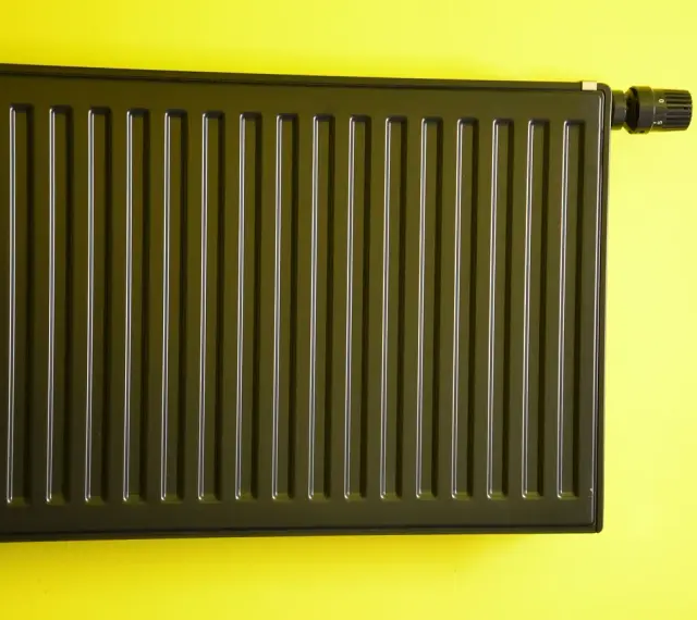 Nowoczesne malowanie grzejnika aluminiowego na ciemny kolor. Grzejnik z termostatem na żółtej ścianie.