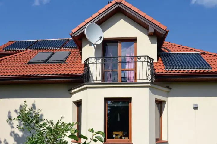 Elegancki wykusz z balkonem i oknami, na dachu panele słoneczne i antenę satelitarną.