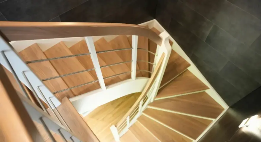Drewniane schody kacze z białymi balustradami i metalowymi poręczami, prowadzące w dół.
