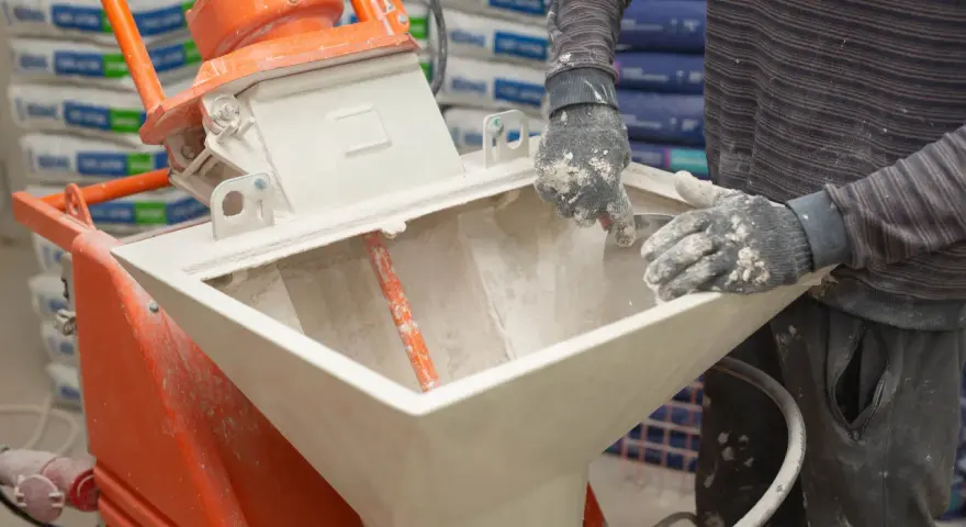 Pracownik zasypuje maszynę do tynków. Sprawdź tynki maszynowe cena za m2 z materiałem.