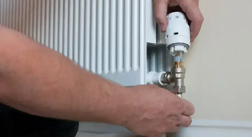 Wymiana zaworu w grzejniku bez spuszczania wody. Ręce majsterkowicza przykręcają nowy zawór termostatyczny.