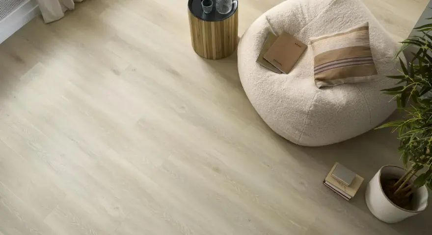 Jasna podłoga z paneli laminowanych lub winylowych imitujących drewno, z pufą, stolikiem i rośliną.