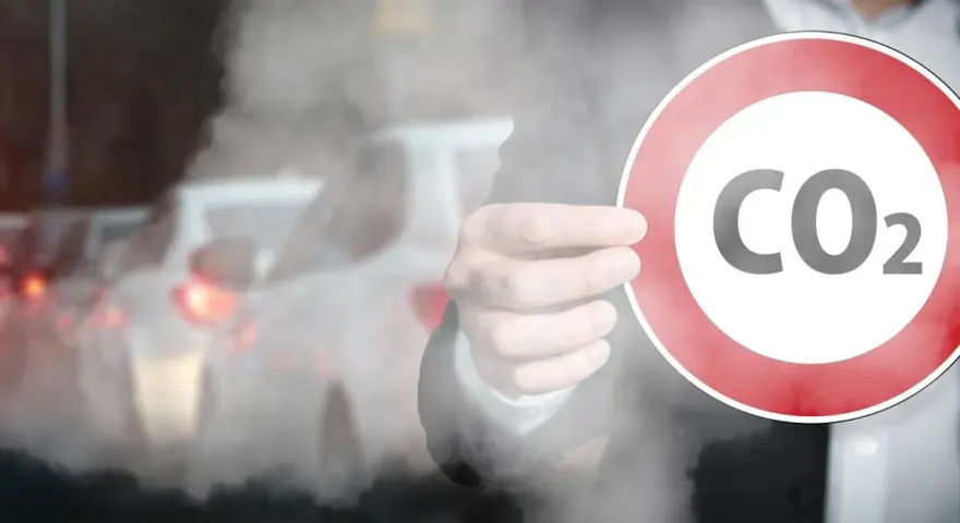 Ręka trzyma znak z napisem CO2 na tle korka ulicznego. Symbolizuje to potrzebę ograniczenia emisji, jak w przypadku certyfikatu CE dla produktów.