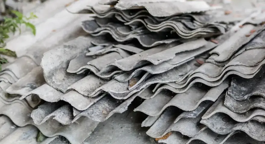 Stos starych, pofalowanych płyt eternitowych, które kiedyś chroniły dachy, teraz leżą na ziemi, czekając na utylizację.