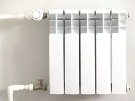 Biały grzejnik z termostatem, podłączony do instalacji rurowej. To efektywne ogrzewanie etażowe, które zapewnia komfort cieplny.