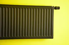 Nowoczesne malowanie grzejnika aluminiowego na ciemny kolor. Grzejnik z termostatem na żółtej ścianie.