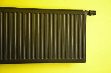 Nowoczesne malowanie grzejnika aluminiowego na ciemny kolor. Grzejnik z termostatem na żółtej ścianie.